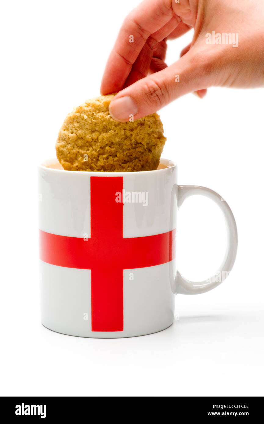 Caucasian hand dunking a biscuit into a white mug with red St Georges cross on the side. Stock Photo