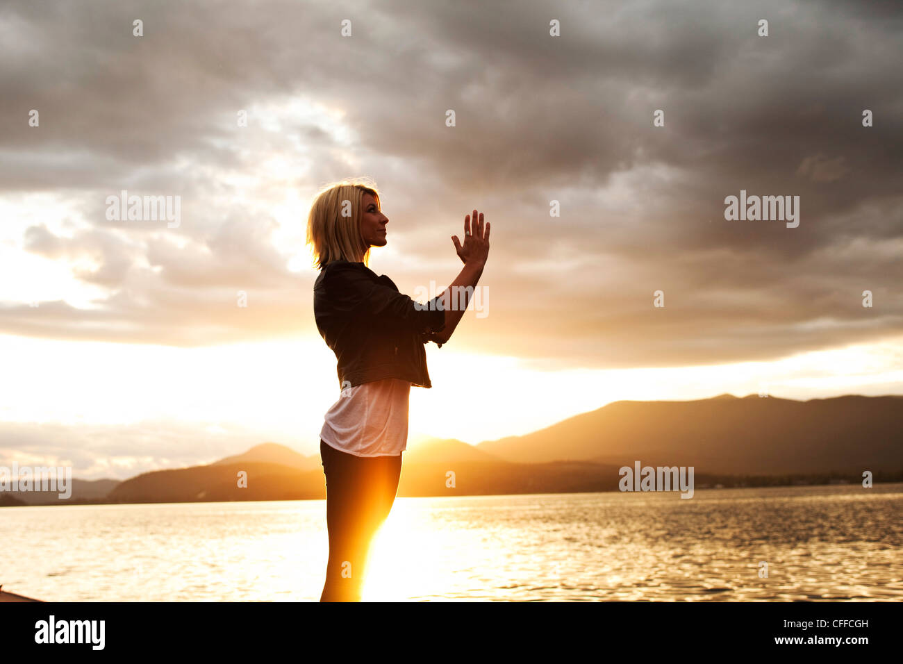 A beautiful young woman meditating as the sunsets over a lake in Idaho. Stock Photo