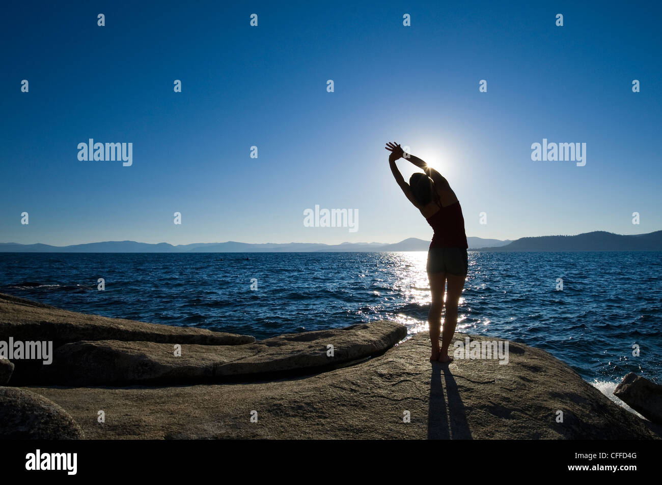 A silhouette of a woman stretching on a granite boulder on the east shore of Lake Tahoe in the summer, NV. Stock Photo
