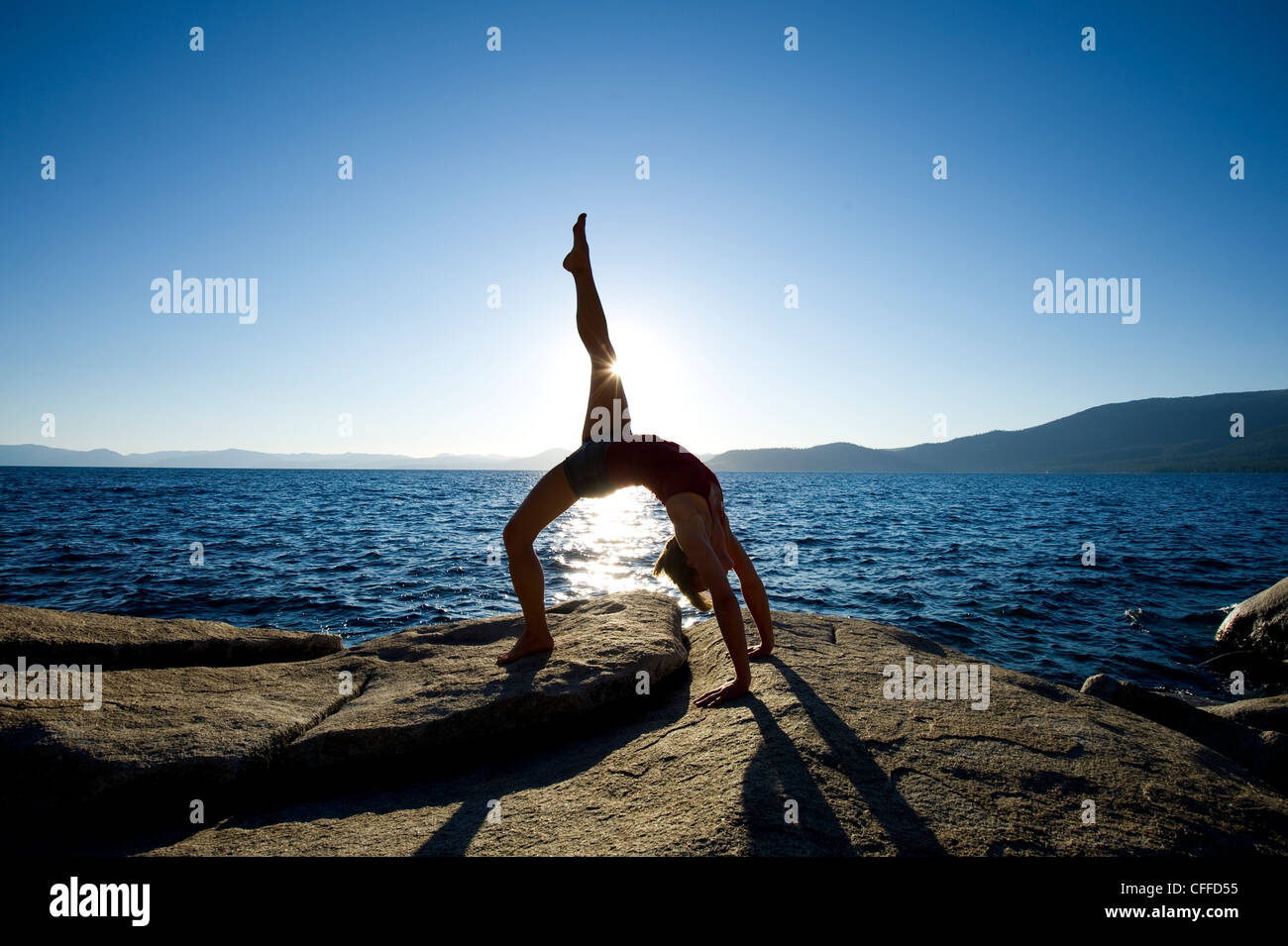 A silhouette of a young woman performing yoga on a granite boulder on the east shore of Lake Tahoe, NV. Stock Photo