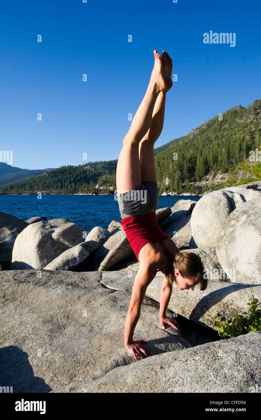 A young woman performs a handstand while doing yoga on granite boulders on the east shore of Lake Tahoe in the summer, NV. Stock Photo