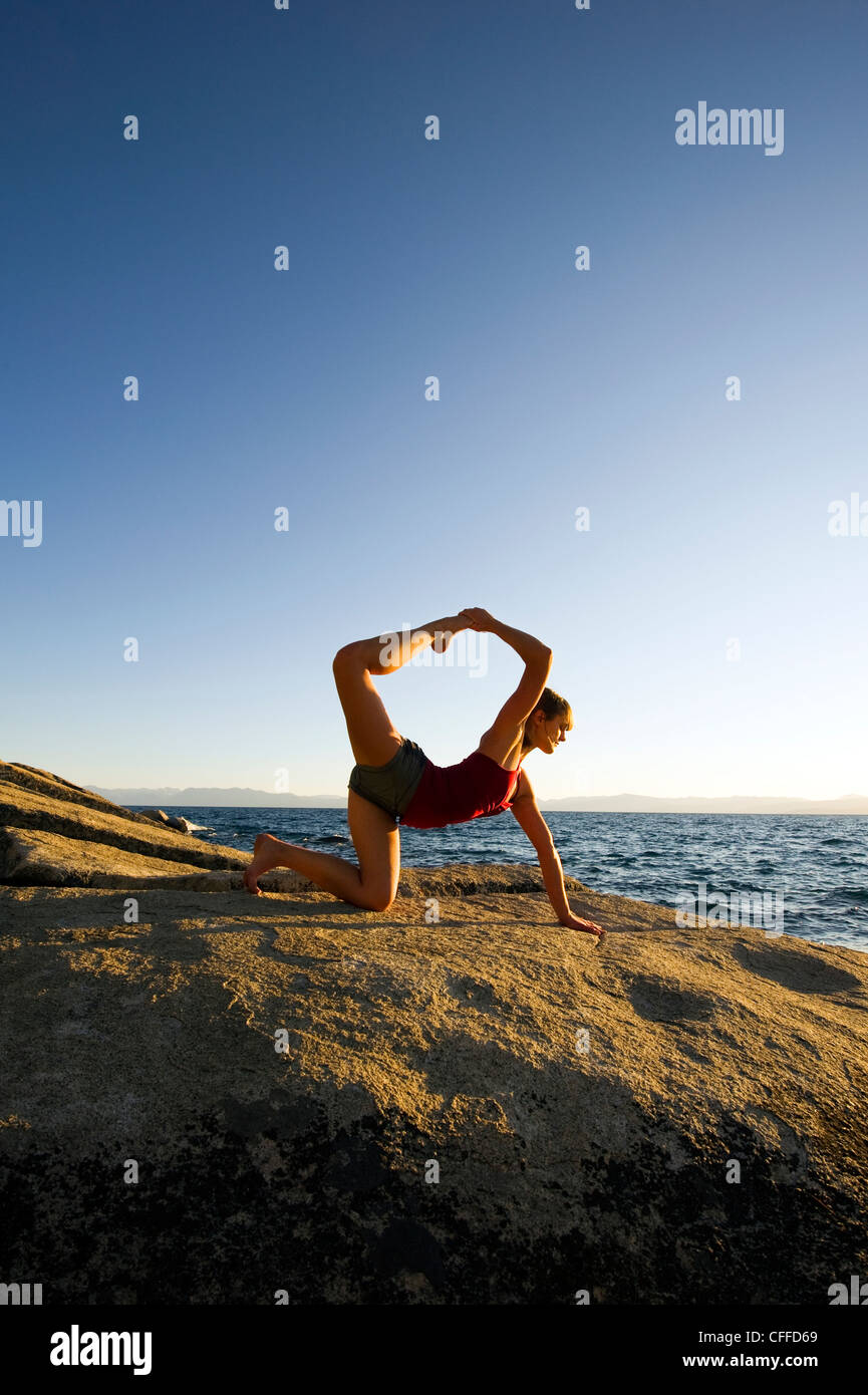 A young woman performs yoga on a granite boulder at sunset on the east shore of Lake Tahoe in the summer, NV. Stock Photo