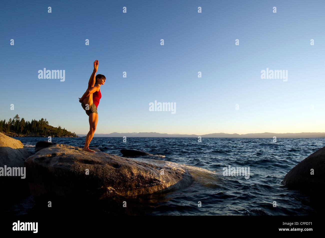 A young woman performs yoga on a granite boulder at sunset on the east shore of Lake Tahoe in the summer, NV. Stock Photo