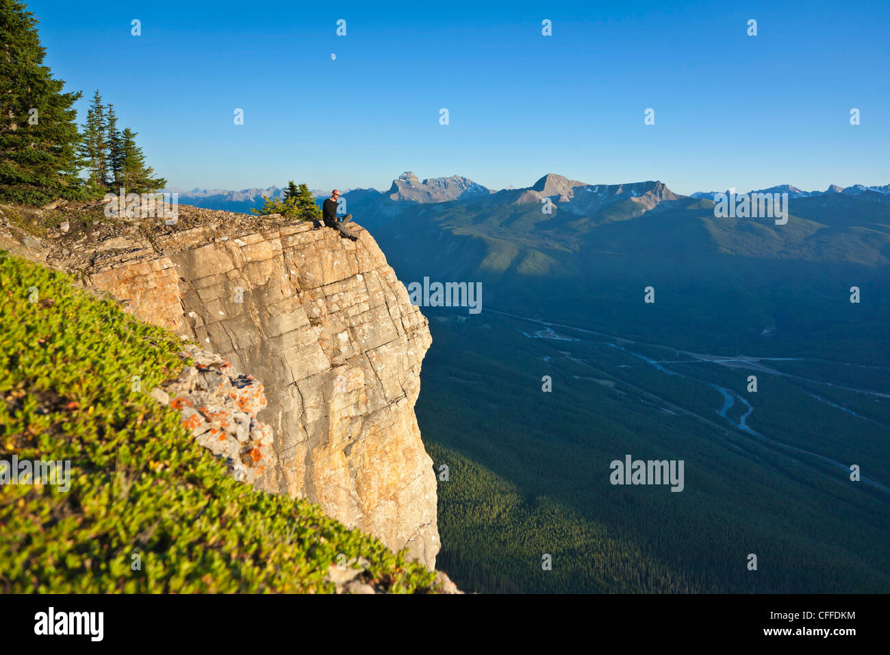 A hiker sits on a cliff edge, Banff National Park, Alberta, Canada. Stock Photo
