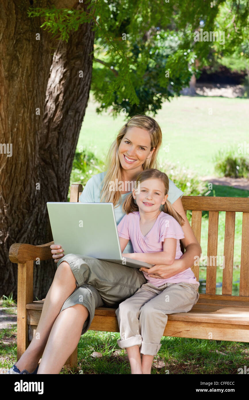 Embracing mother and daughter sit on the park bench with a laptop in ...
