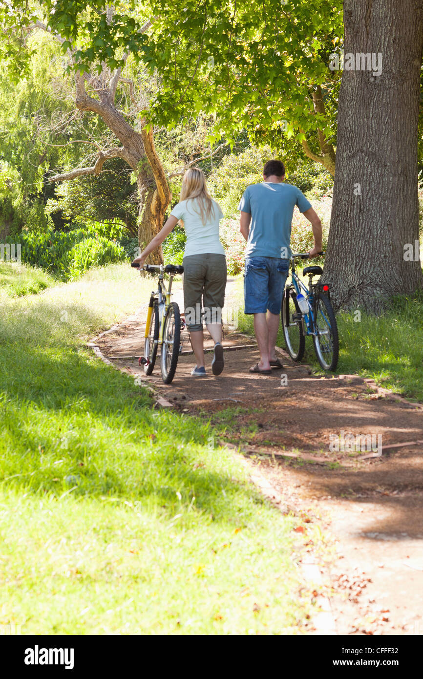 Back view of couple wheeling their bikes through a park Stock Photo