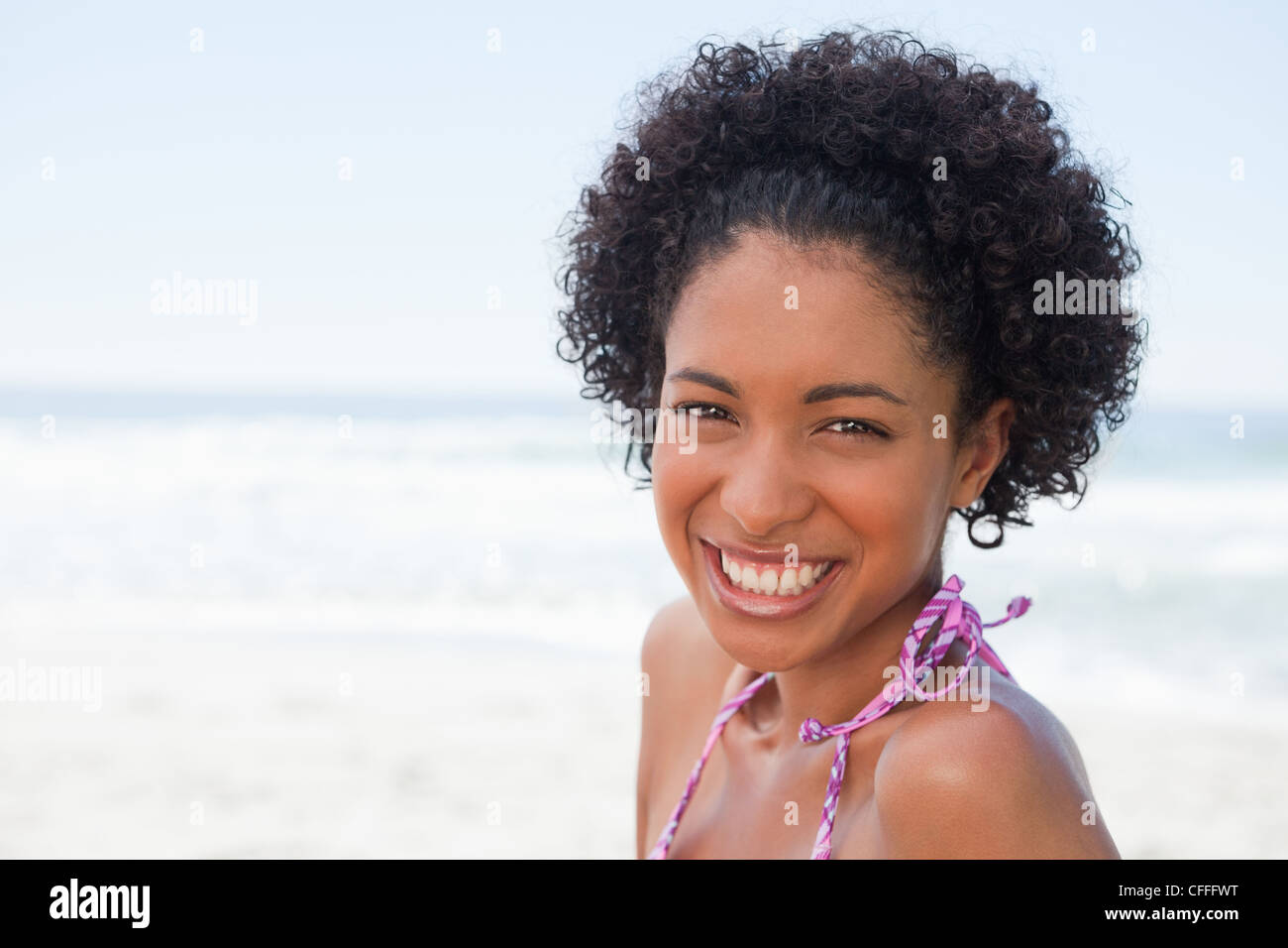 Young woman looking at the camera while standing in front of the ocean ...
