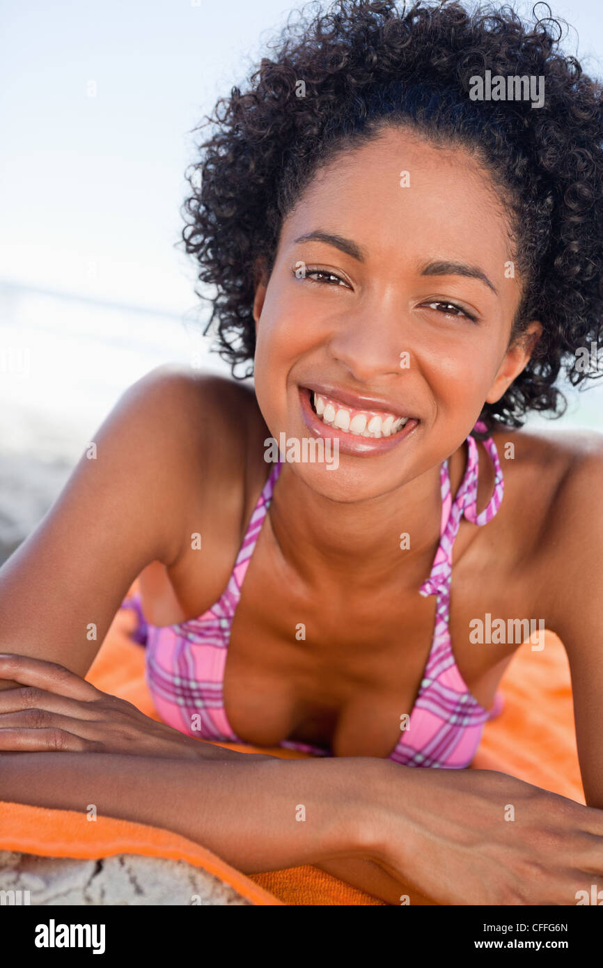 Young woman lying on her beach towel while showing a beaming smile Stock Photo
