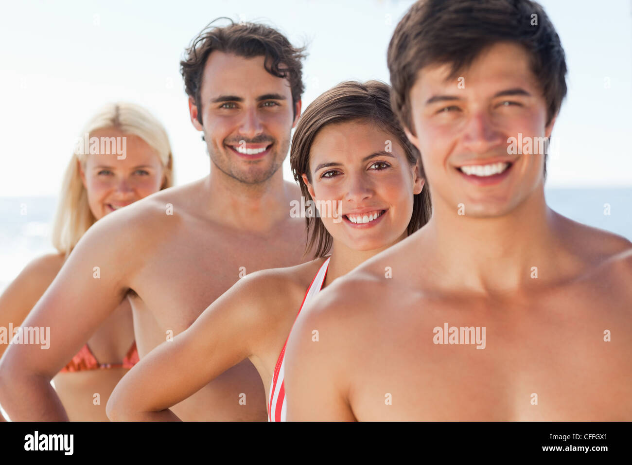 Four friends with happy expressions smiling as they stand behind each other Stock Photo