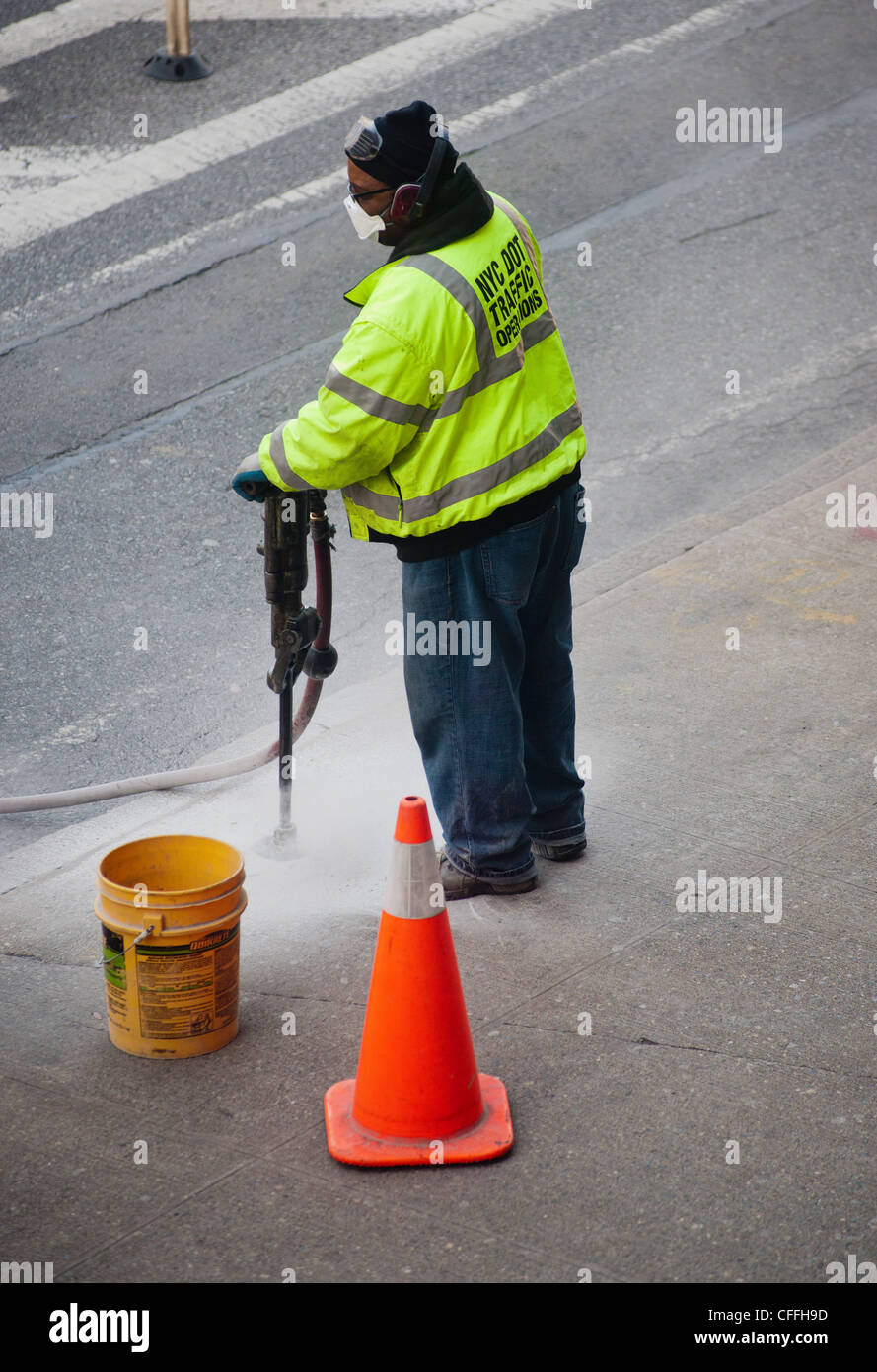 NYC Dept. of Transportation worker uses a jackhammer to break up a concrete sidewalk for a replacement sign project Stock Photo