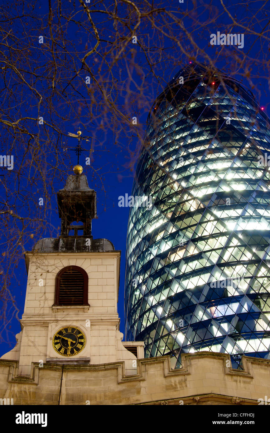 Swiss Re Building 30 St Mary Axe also known as the Gherkin at night with tower of St Helen's Bishopsgate London England UK Stock Photo