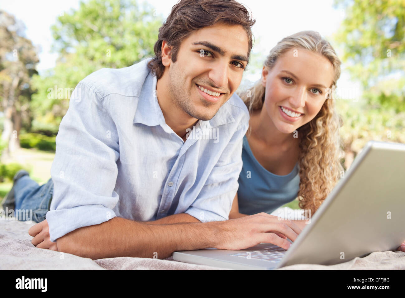 Smiling couple lying on their lawn with their laptop Stock Photo - Alamy