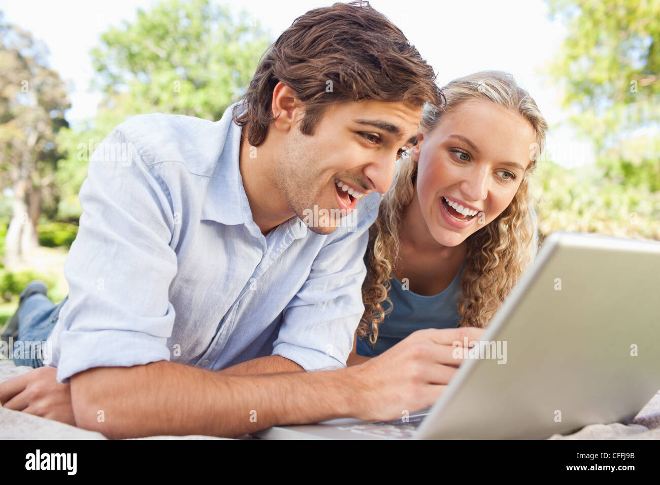 Happy couple lying on the lawn with their laptop Stock Photo - Alamy