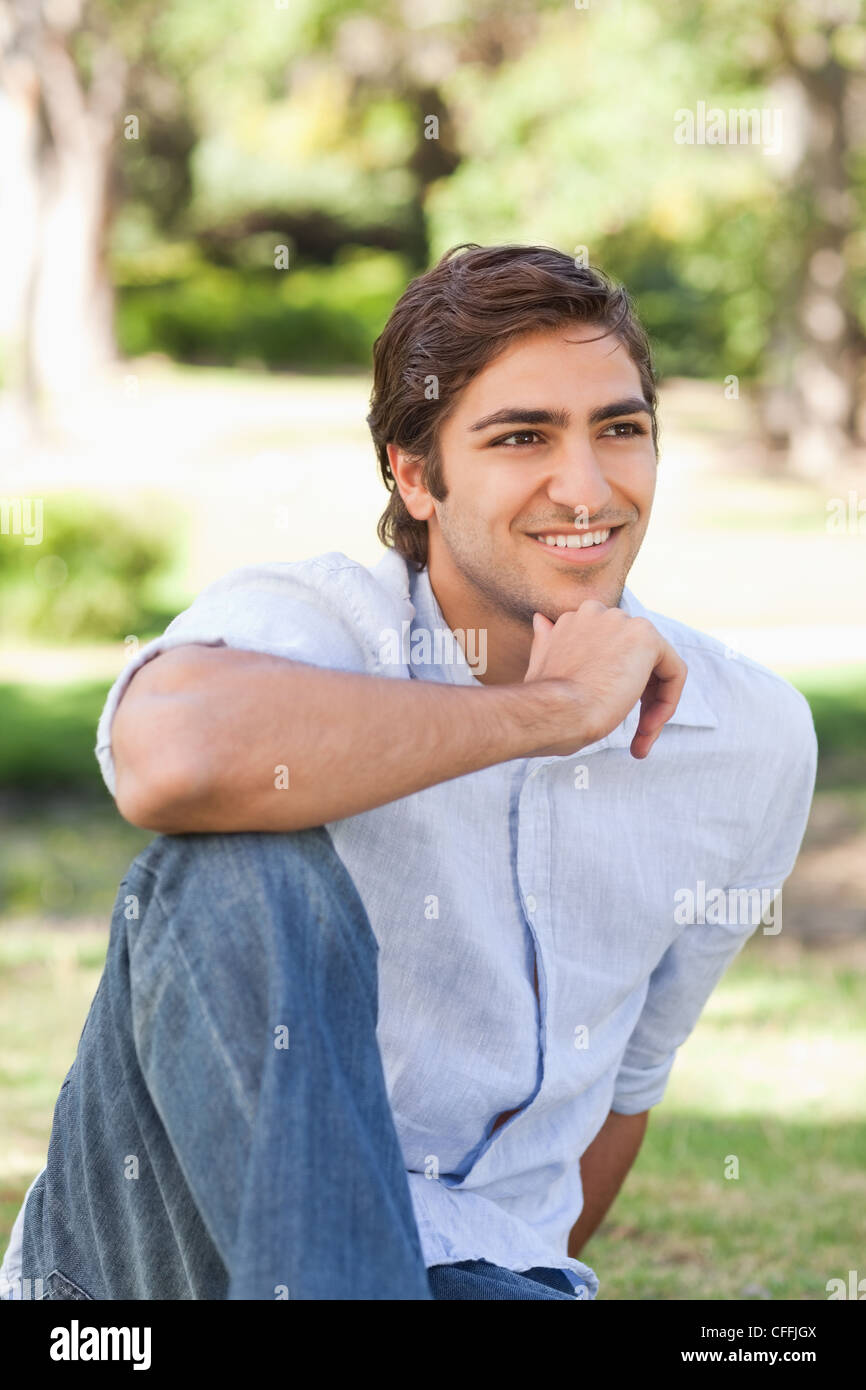 Smiling man thoughtfully sitting on the lawn Stock Photo