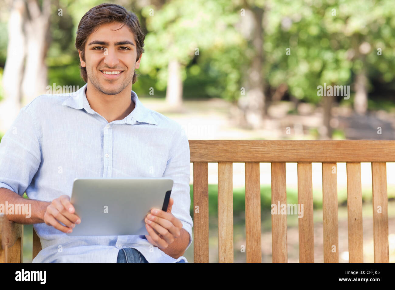 Smiling man with his tablet sitting on a park bench Stock Photo - Alamy