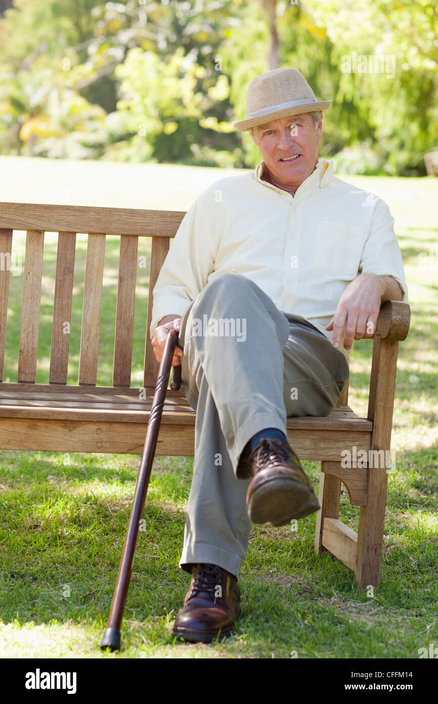 Man smiling while siting on a bench as he hold a cane Stock Photo