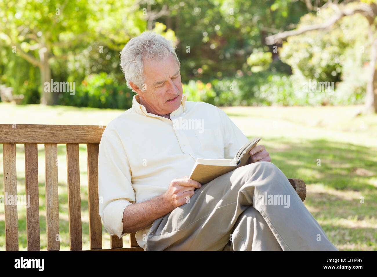 Man seriously reading a book as he sits on a bench Stock Photo