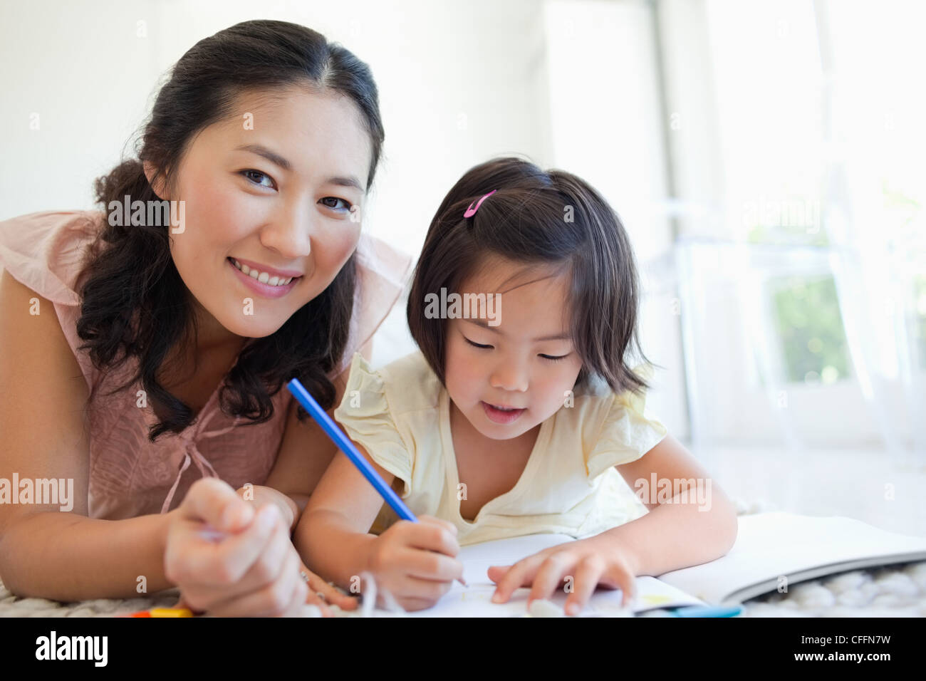 Mother looks ahead as her daughter continues on with colouring Stock Photo