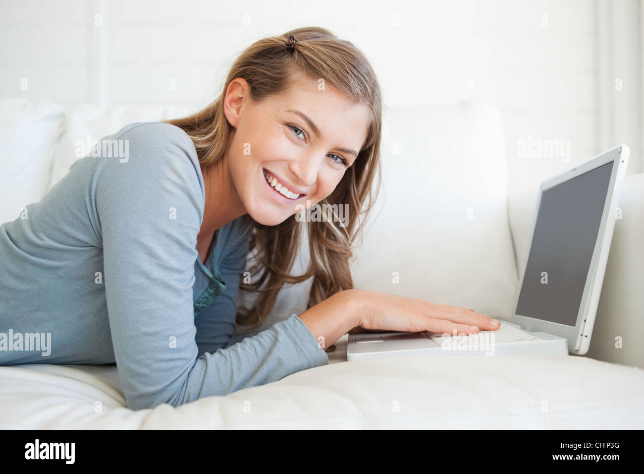 A smiling woman looks forward as she uses her laptop on the couch Stock ...