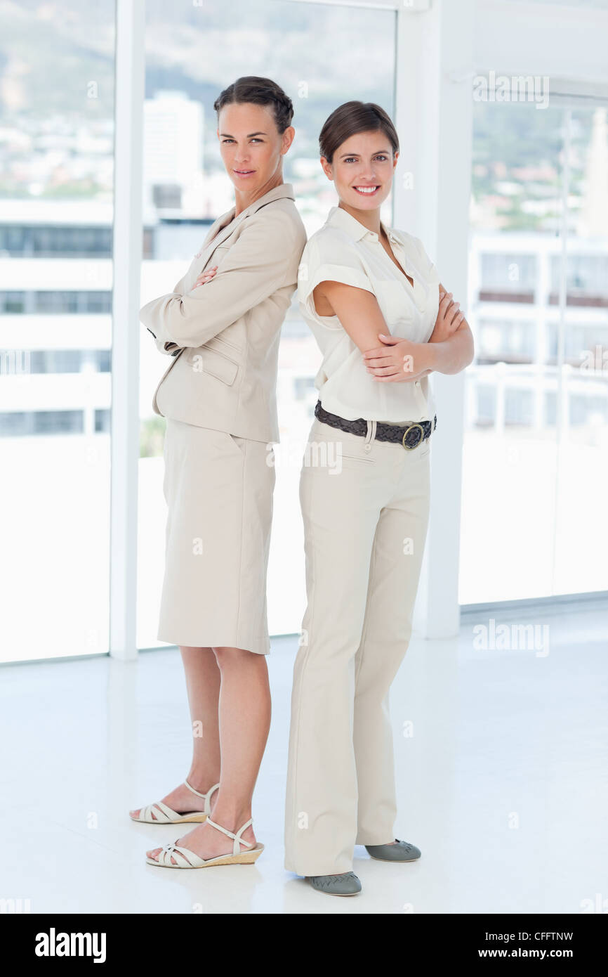 Businesswomen with arms folded standing back to back Stock Photo