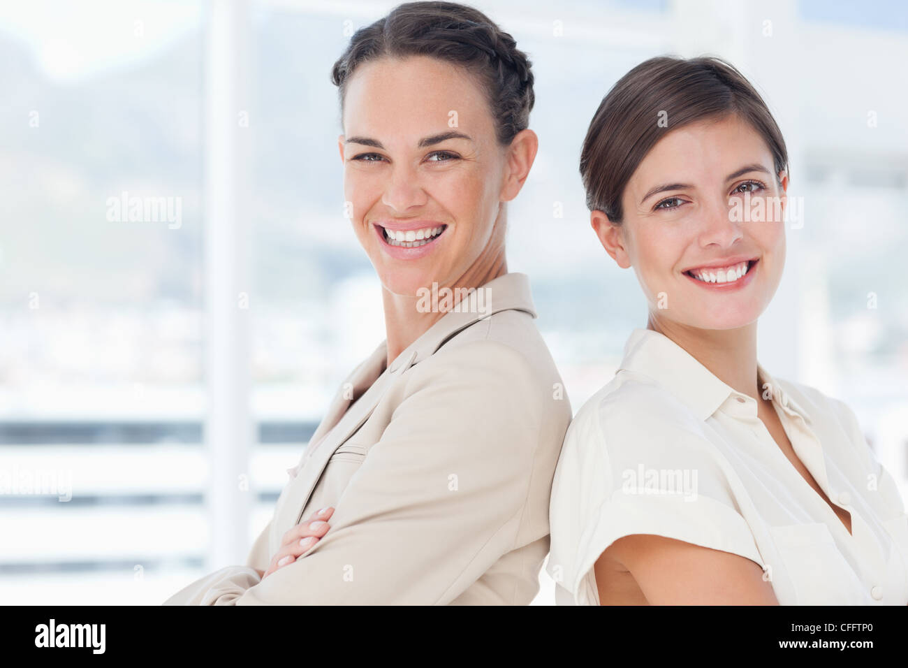 Smiling businesswomen with arms folded standing back to back Stock Photo