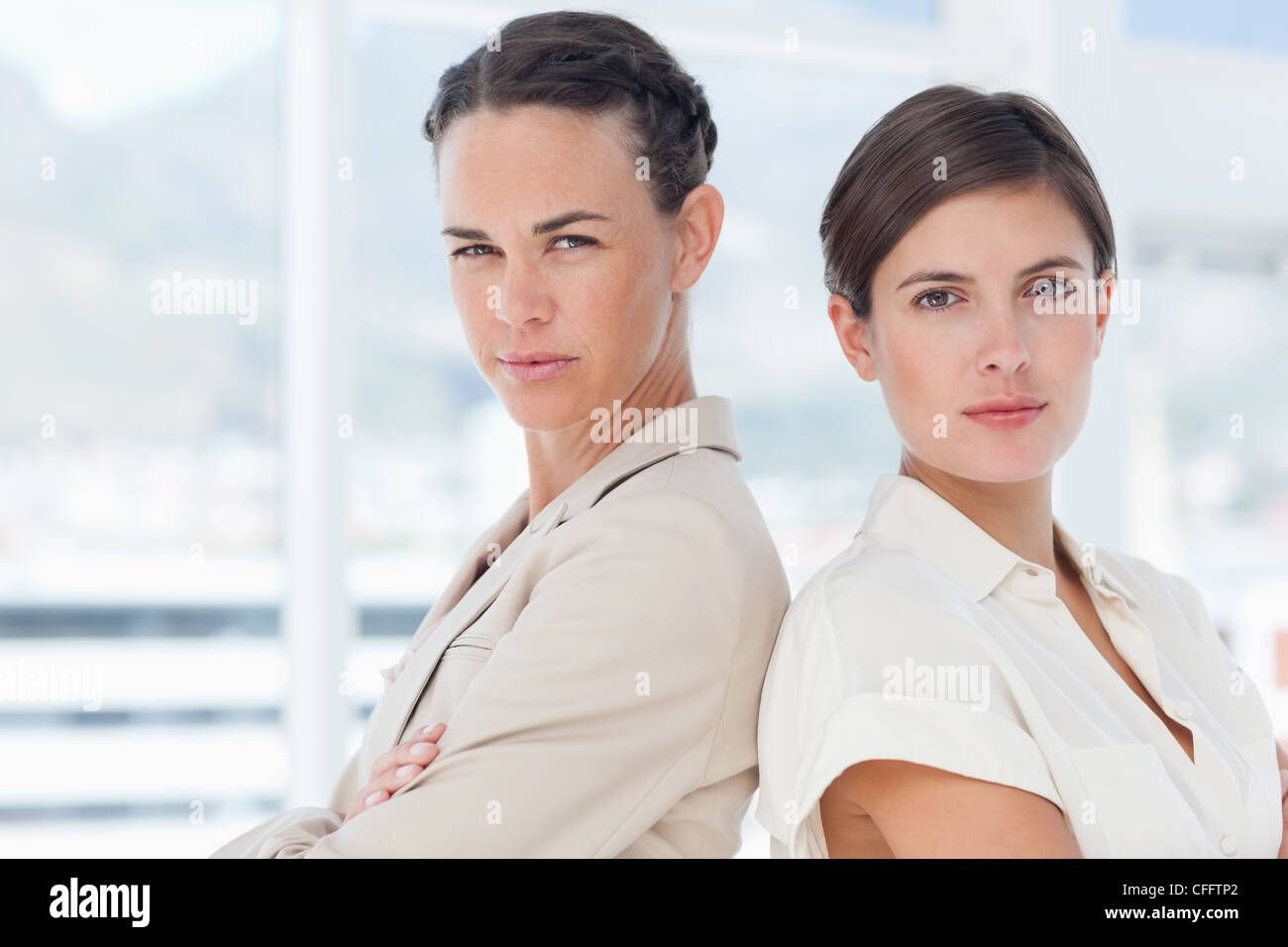 Serious businesswomen with arms folded standing back to back Stock Photo