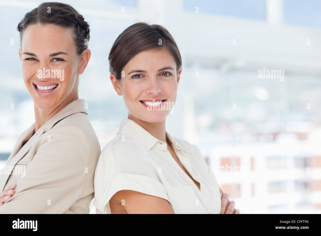 Smiling businesswomen with arms crossed standing back to back Stock Photo