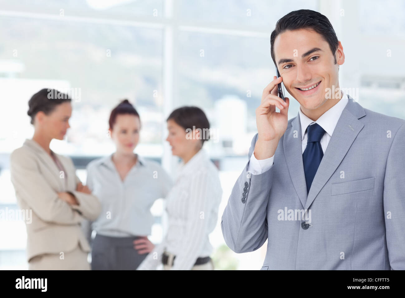 Smiling businessman on his cellphone with colleagues behind him Stock ...