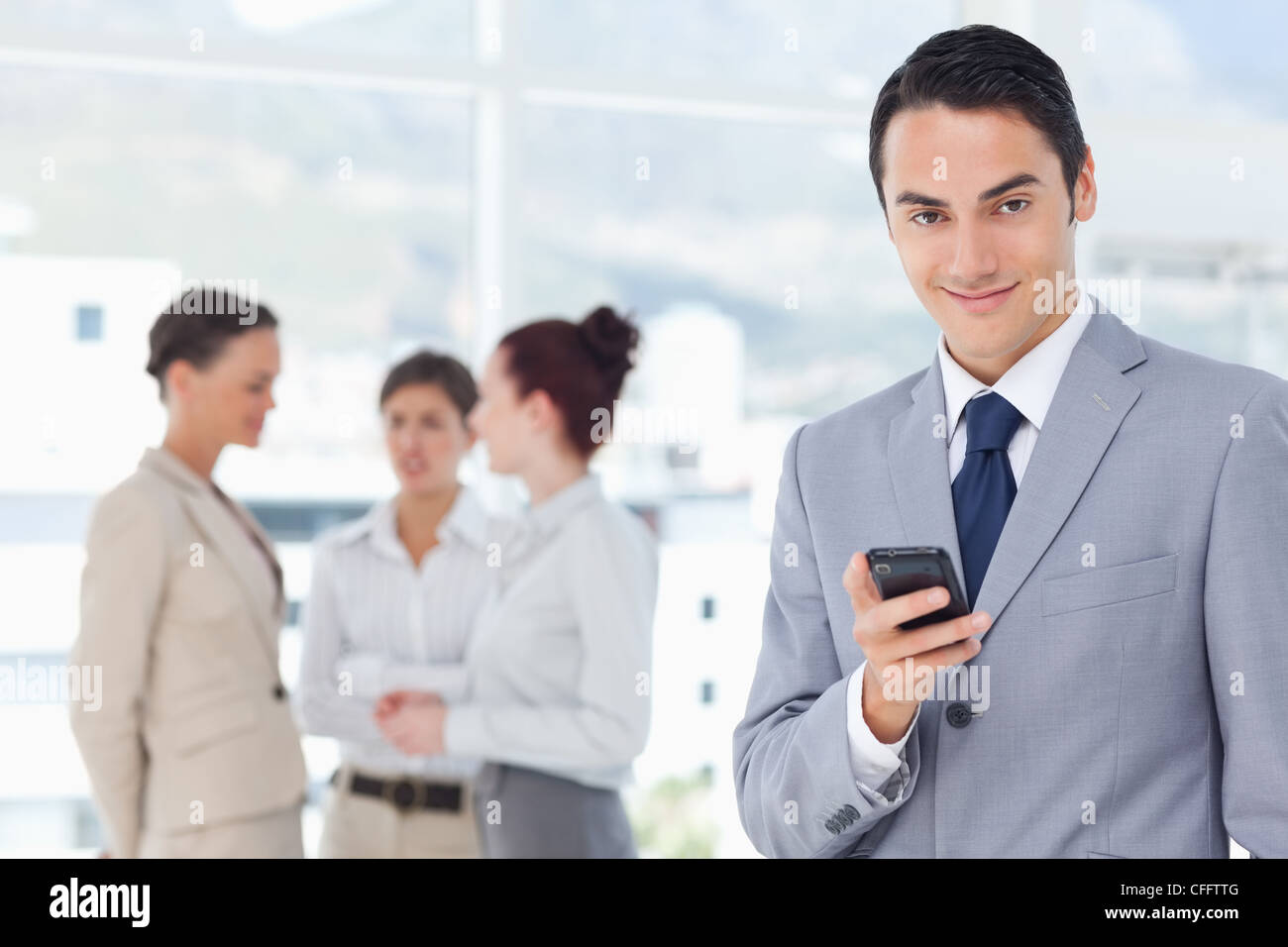 Smiling businessman with cellphone and colleagues behind him Stock ...