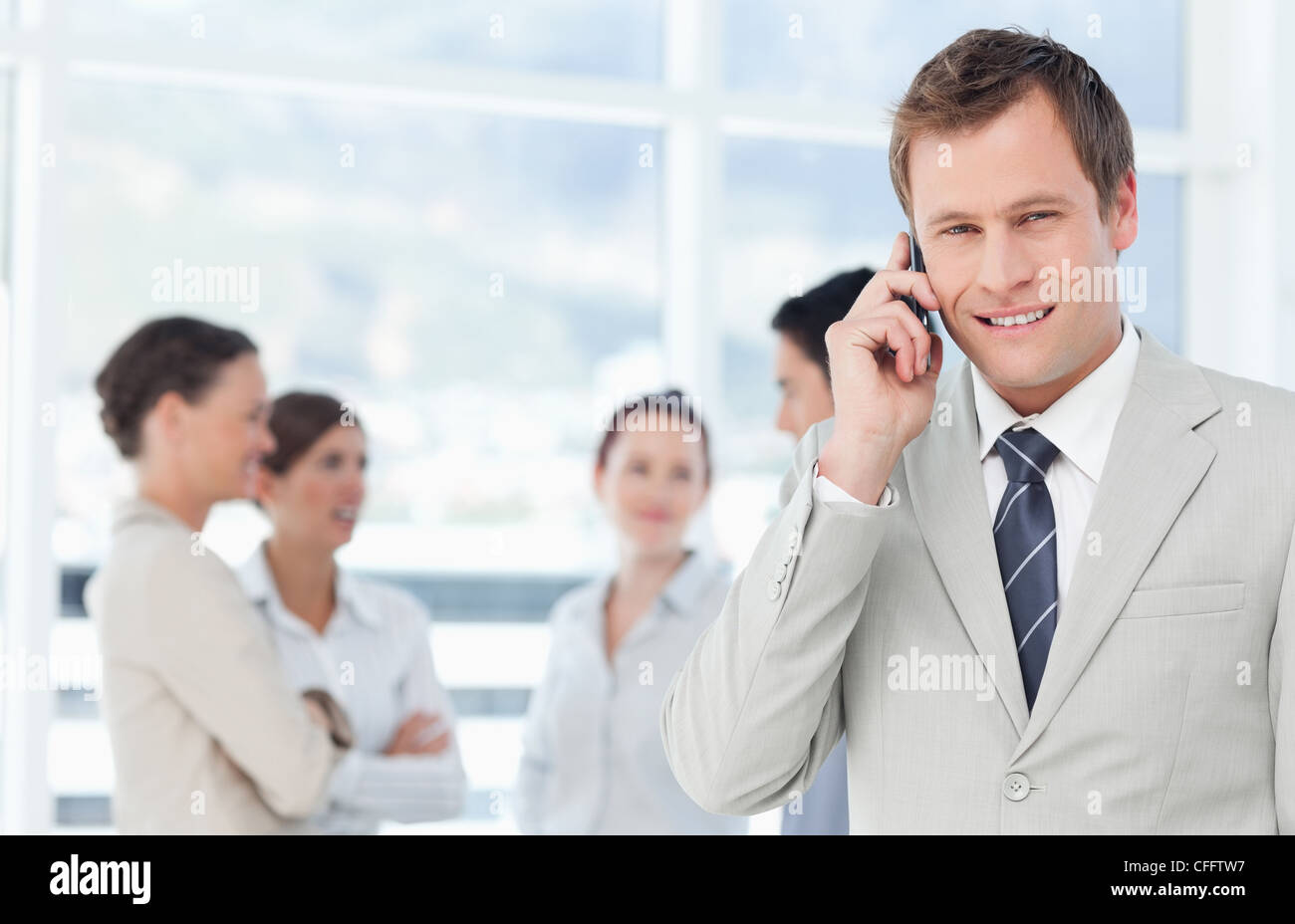 Smiling salesman on his cellphone with colleagues behind him Stock ...
