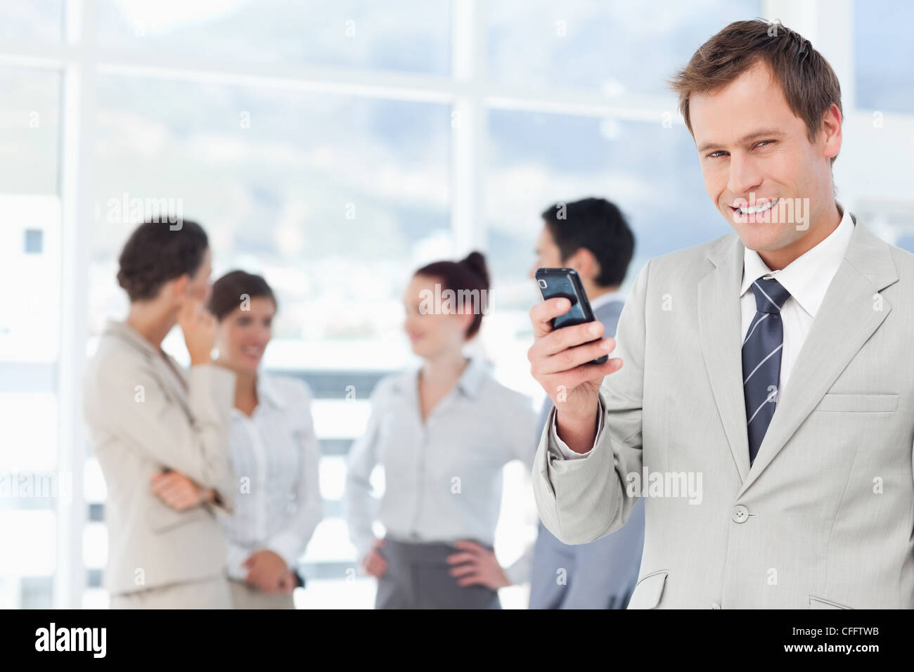 Smiling salesman with his cellphone and colleagues behind him Stock ...