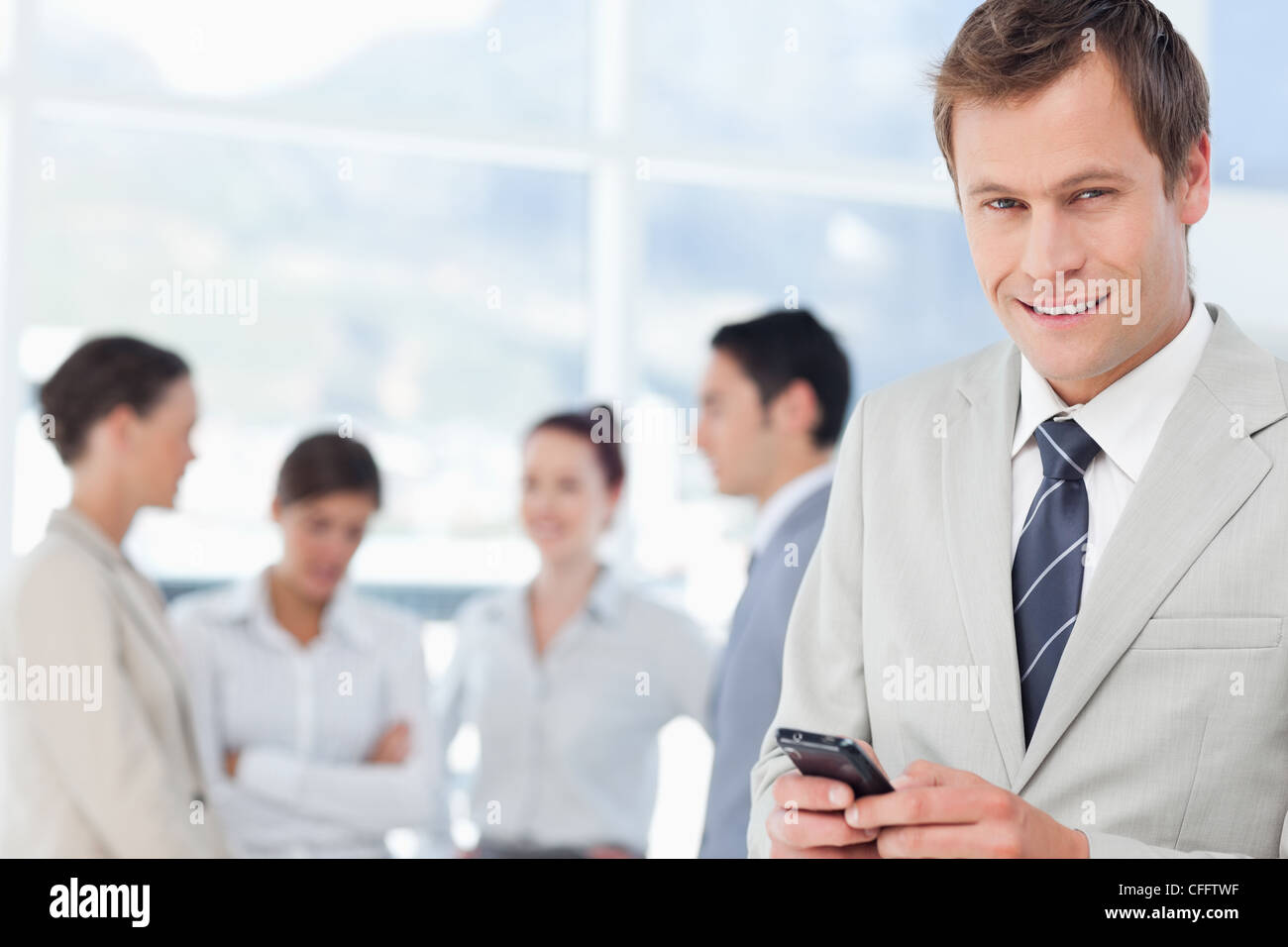 Smiling salesman with his mobile phone and colleagues behind him Stock ...
