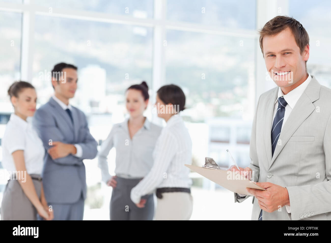 Smiling salesman with clipboard and colleagues behind him Stock Photo ...