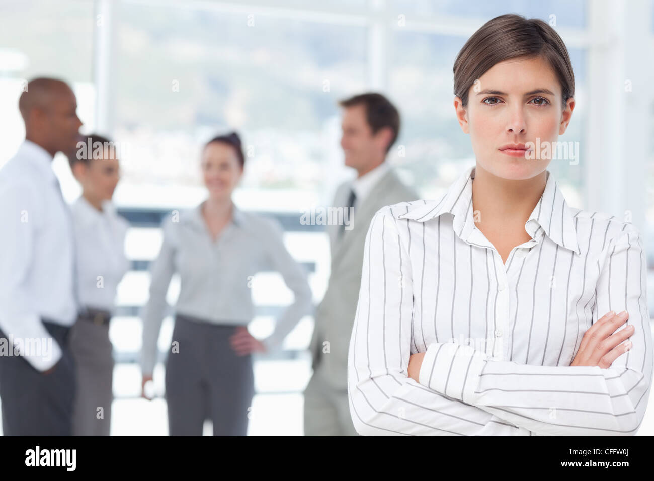 Saleswoman with arms folded and colleagues behind her Stock Photo
