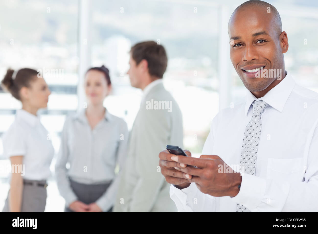Smiling salesman with his cellphone and associates behind him Stock ...