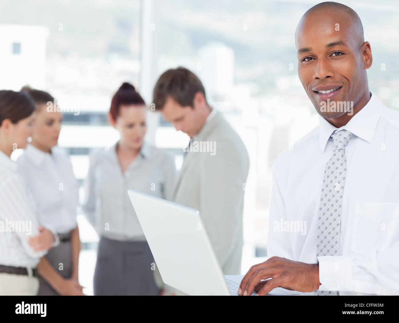 Smiling salesman with his laptop and associates behind him Stock Photo ...