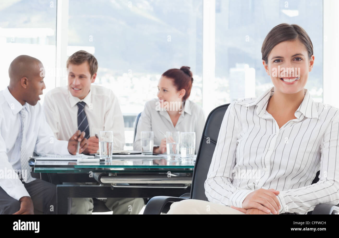 Smiling saleswoman with meeting being held behind her Stock Photo