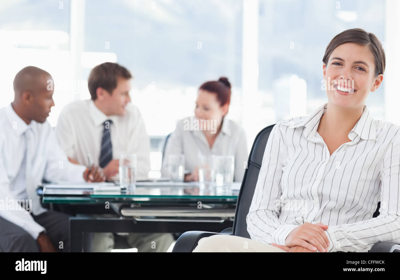 Smiling businesswoman with meeting being held behind her Stock Photo