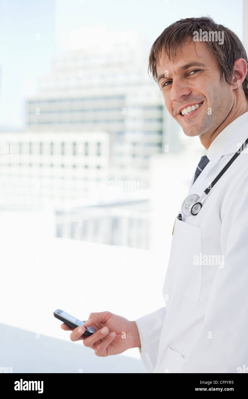 Smiling doctor standing in front of the window while sending a text Stock Photo
