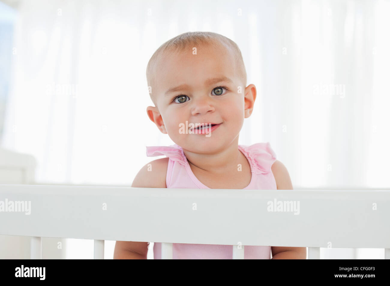 Lovely baby looking at the camera while standing in her bed Stock Photo