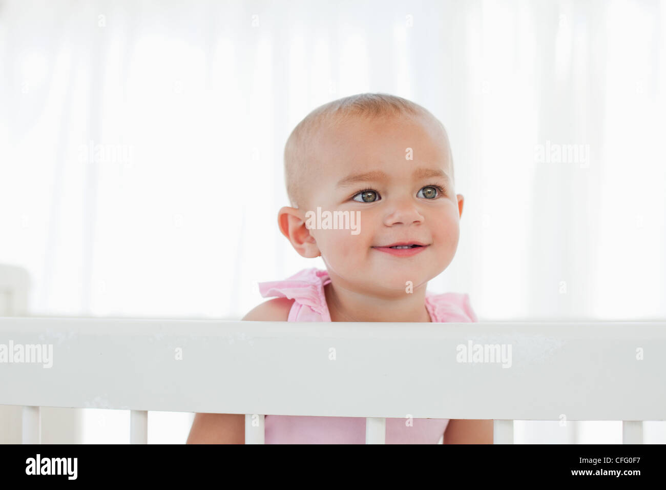 Smiling baby looking towards the side while standing in her bed Stock Photo