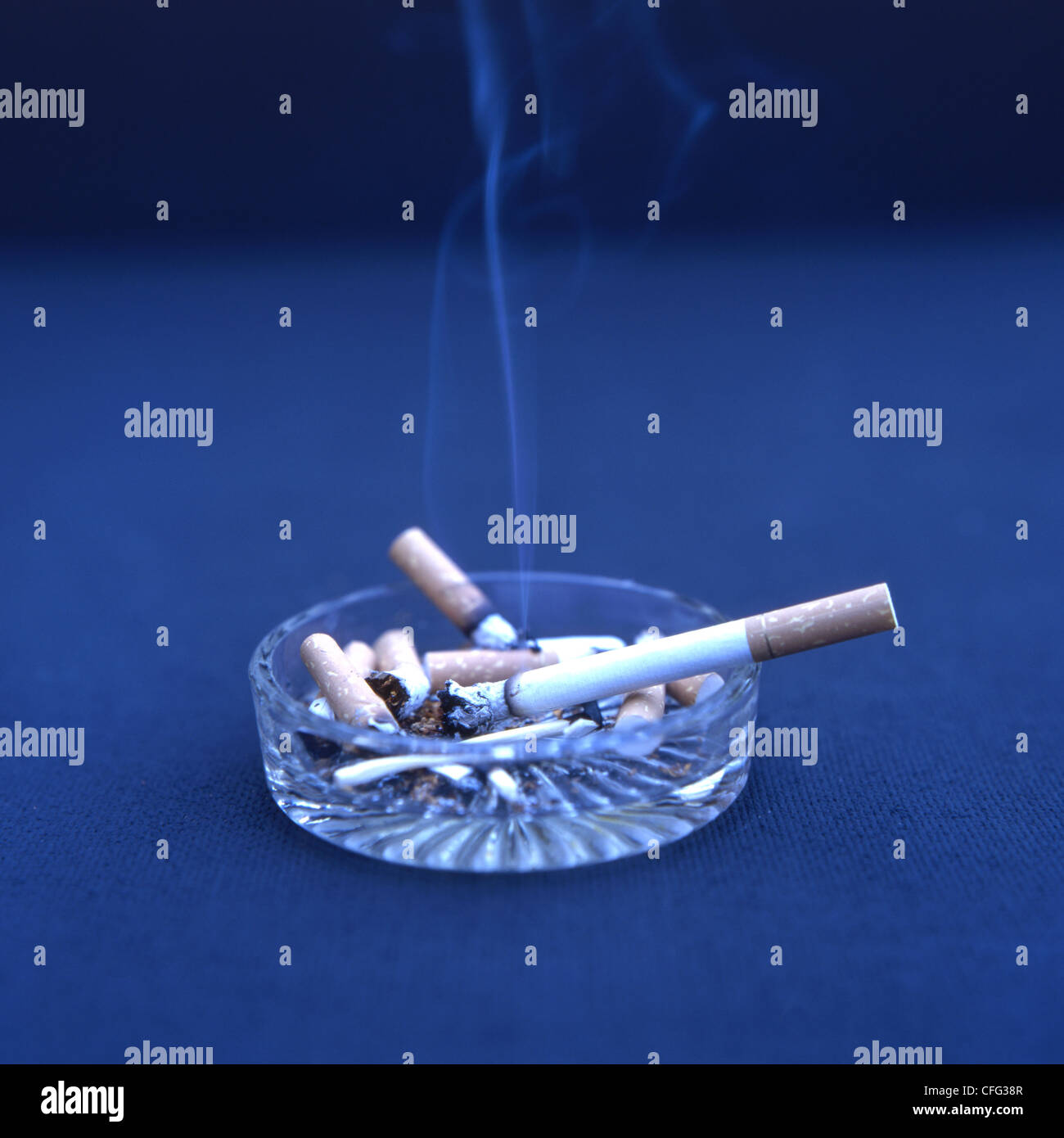 Filter tipped cigarettes in ashtray with one alight and smoking Stock