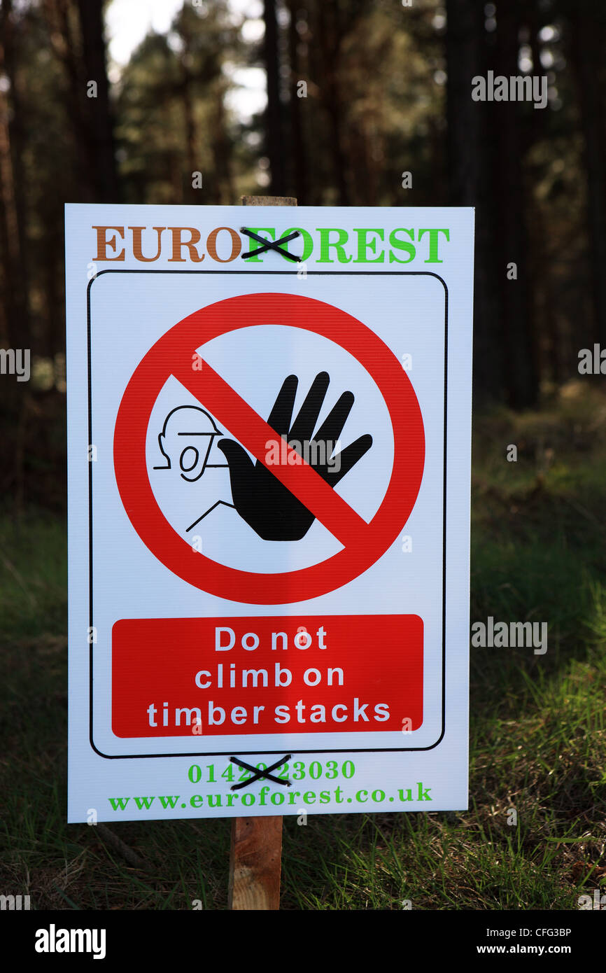 Warning sign advising not to climb on timber stacks in woodland area with felled trees Stock Photo