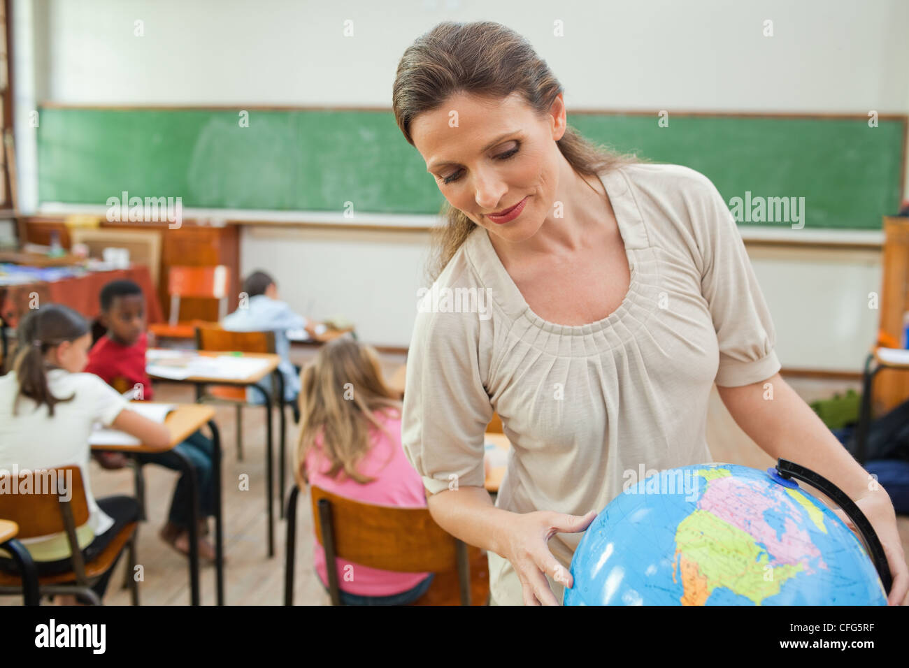 Teacher looking at globe in classroom Stock Photo