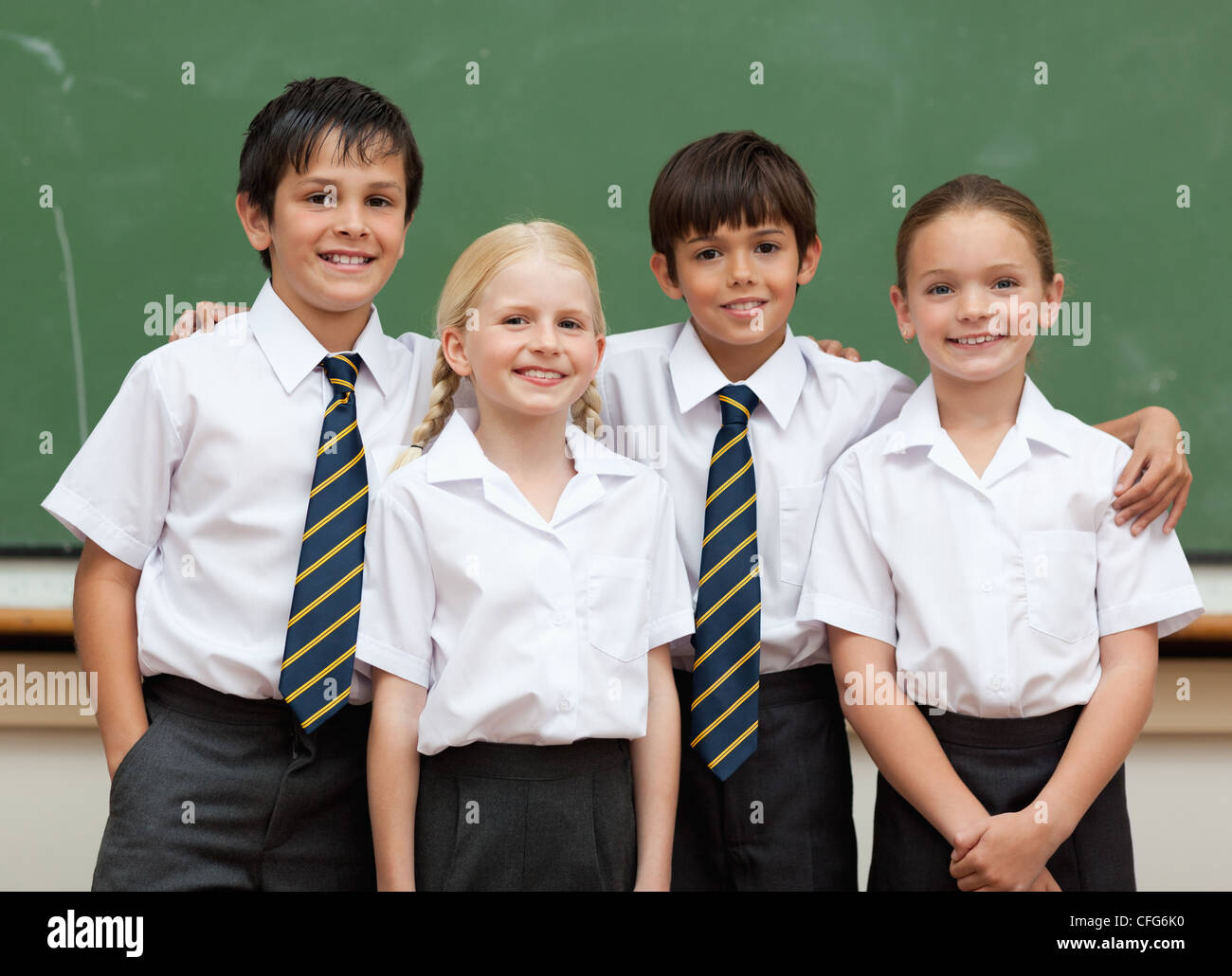 Smiling schoolfellows in school uniforms standing in front of blackboard Stock Photo