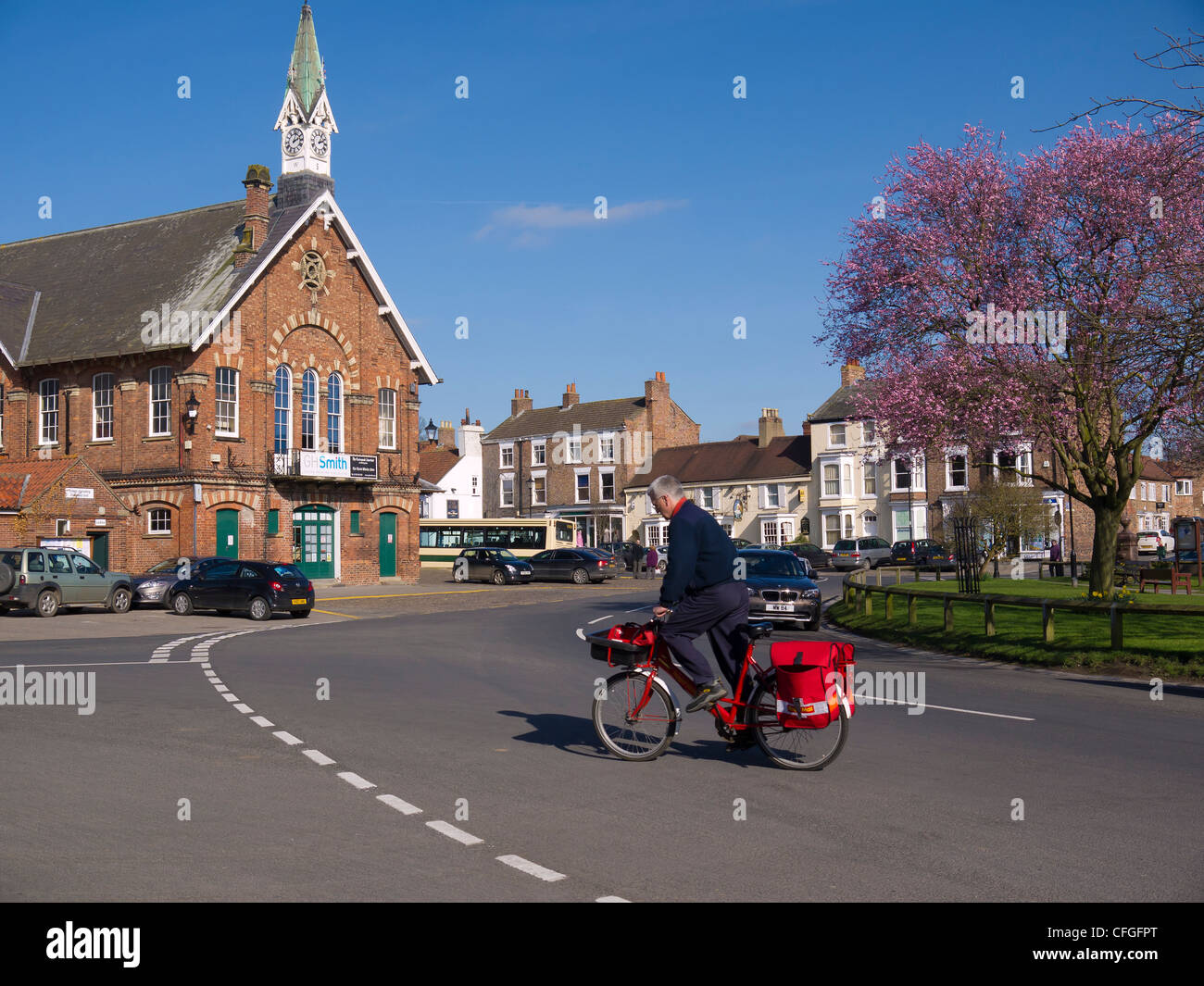 A Postman on a bicycle crosses the Market Square Easingwold North Yorkshire England in spring Stock Photo