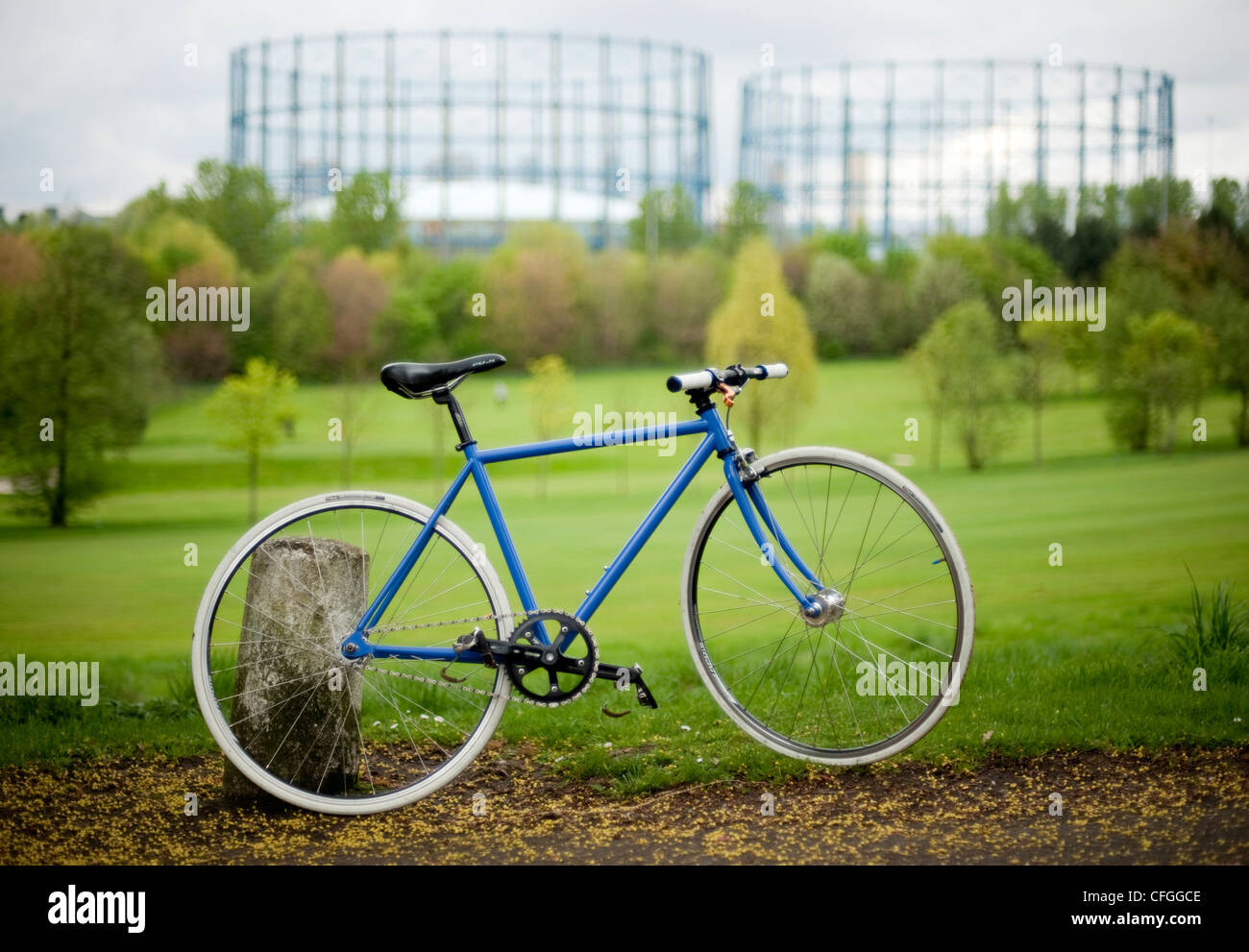 A blue and white fixed wheel bicycle in a park in autumn in front of gas towers Stock Photo