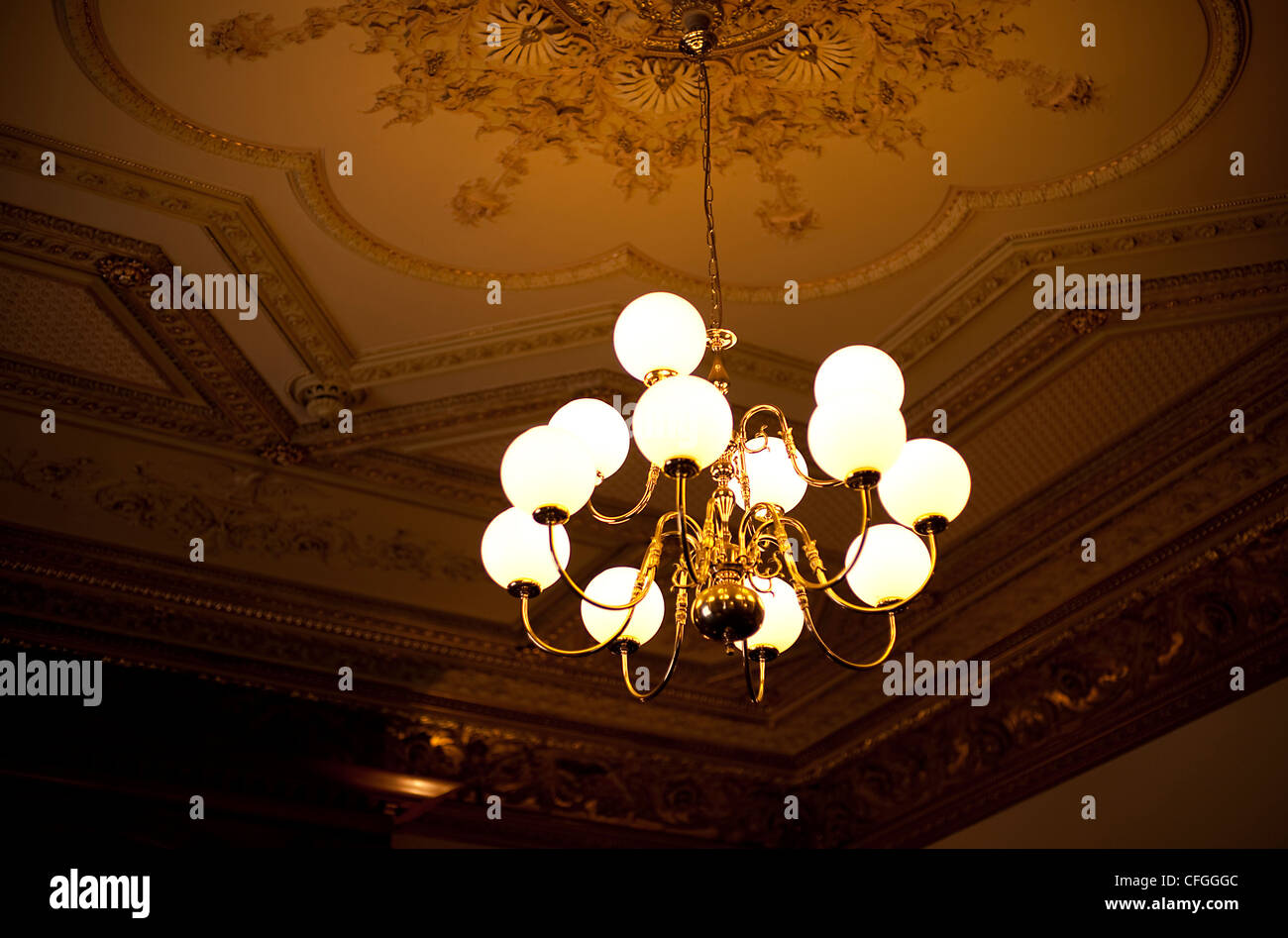 A glass domed light hangs from an ornately decorated ceiling at a