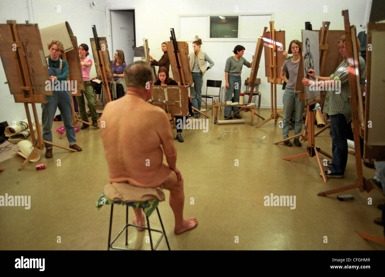 A class of girl art students painting a naked elderly male model