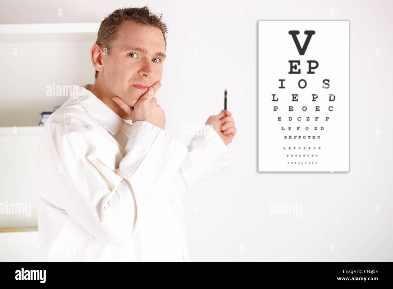 Serious male oculist doctor with an eye chart behind him. Worried about examined patient sight. Stock Photo